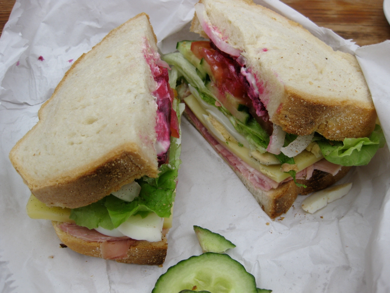 A white bread sandwich cut in half with an almost impossible quantity of ingredients inside. Ham, egg, onion, lettuce, tomato, cucumber, mayonnaise and beetroot. 