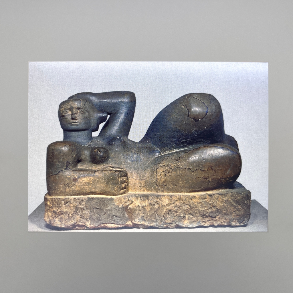 Postcard picture of Henry Moores reclining figure statue. A slightly abstract woman lying down with one elbow on the floor the other casually behind her head. She seems relaxed and thoughtful. 