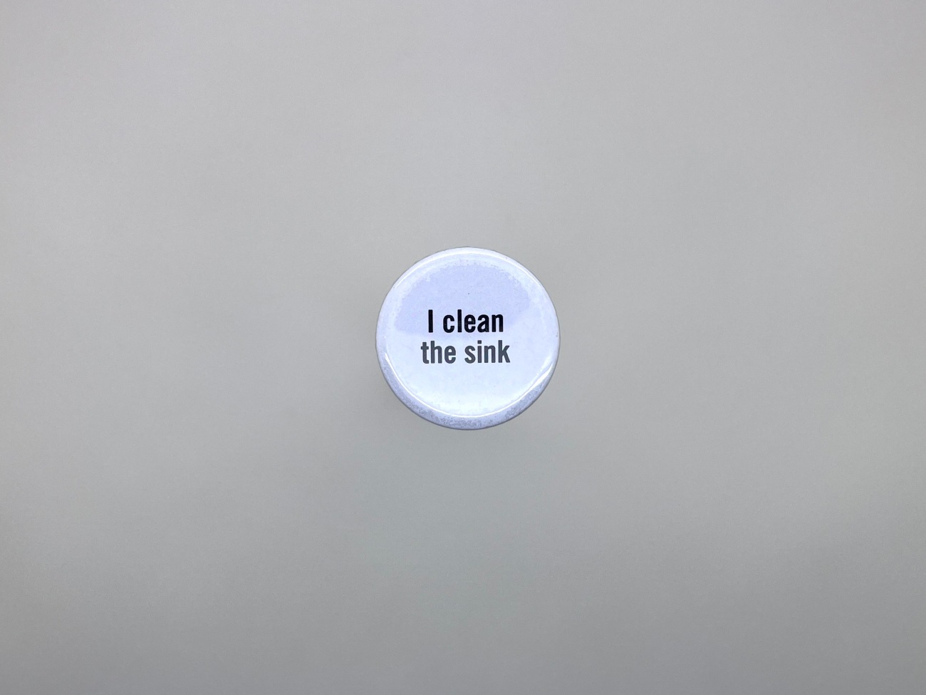 A small white badge (which American's call pins, which feels odd to a British ear).  It  reads 'I clean the sink'. 