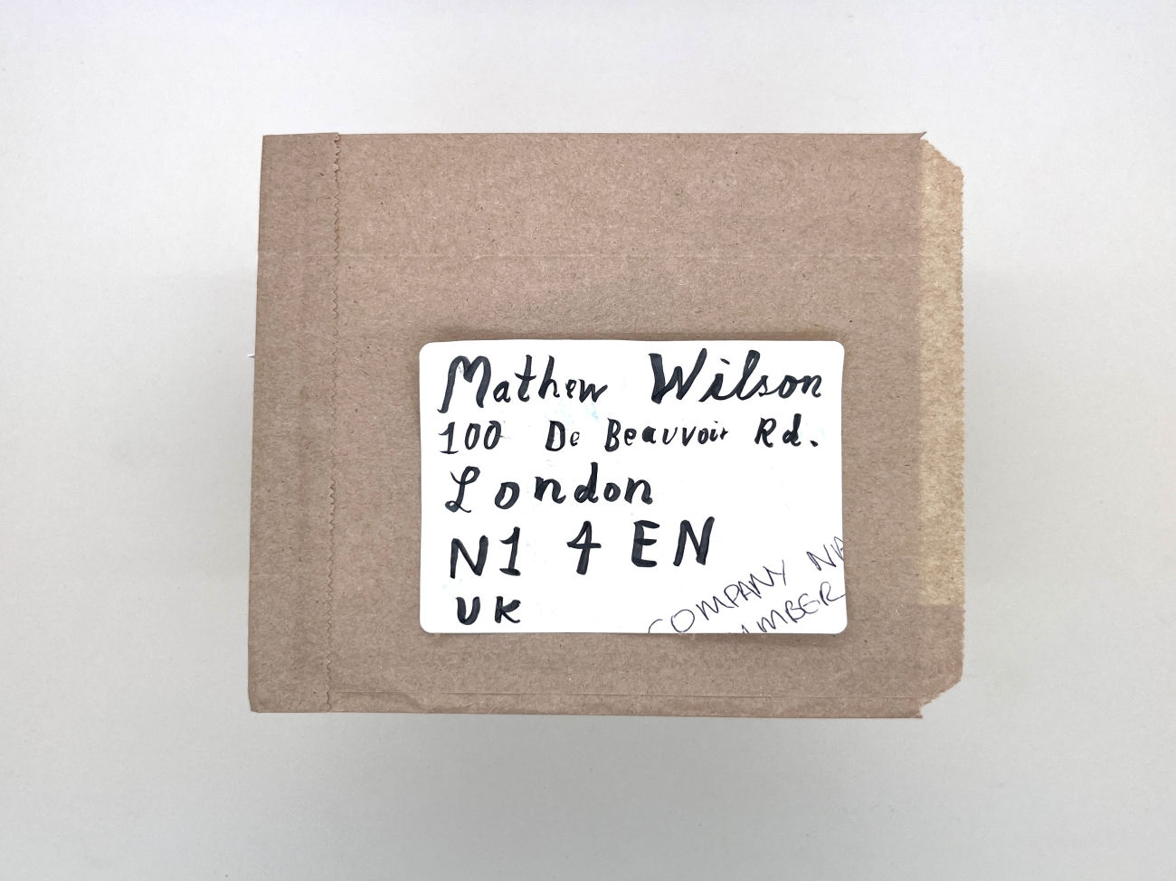 A brown paper with the address sticker from an envelope on it, a with friendly hand written address to Mathew Wilson, 100 De Beauvoir Rd, London, N1 4EN, UK