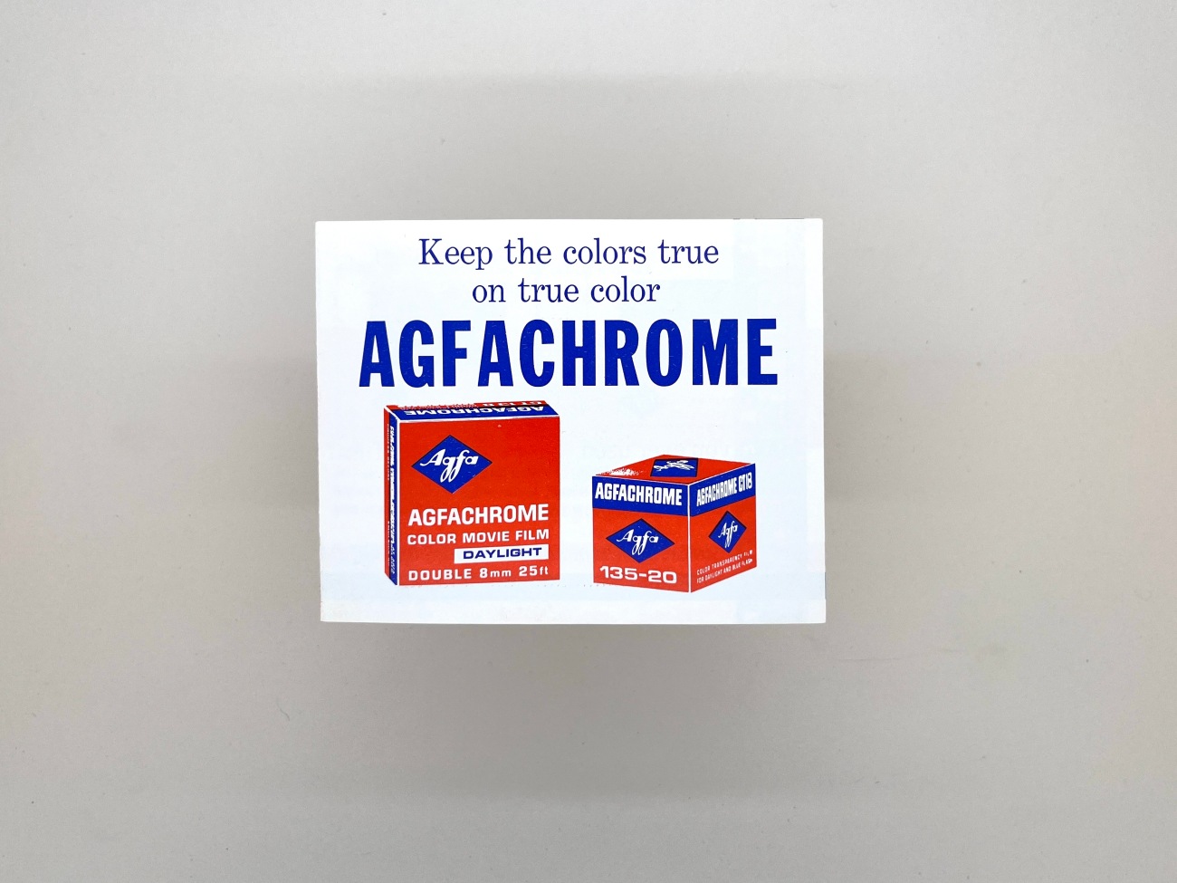 A blue and red illustrated image of two boxes of Agfachrome film. One Double 8mm the other 135-20. The words Keep the colors true on tru color Agfachrome are above the boxes.