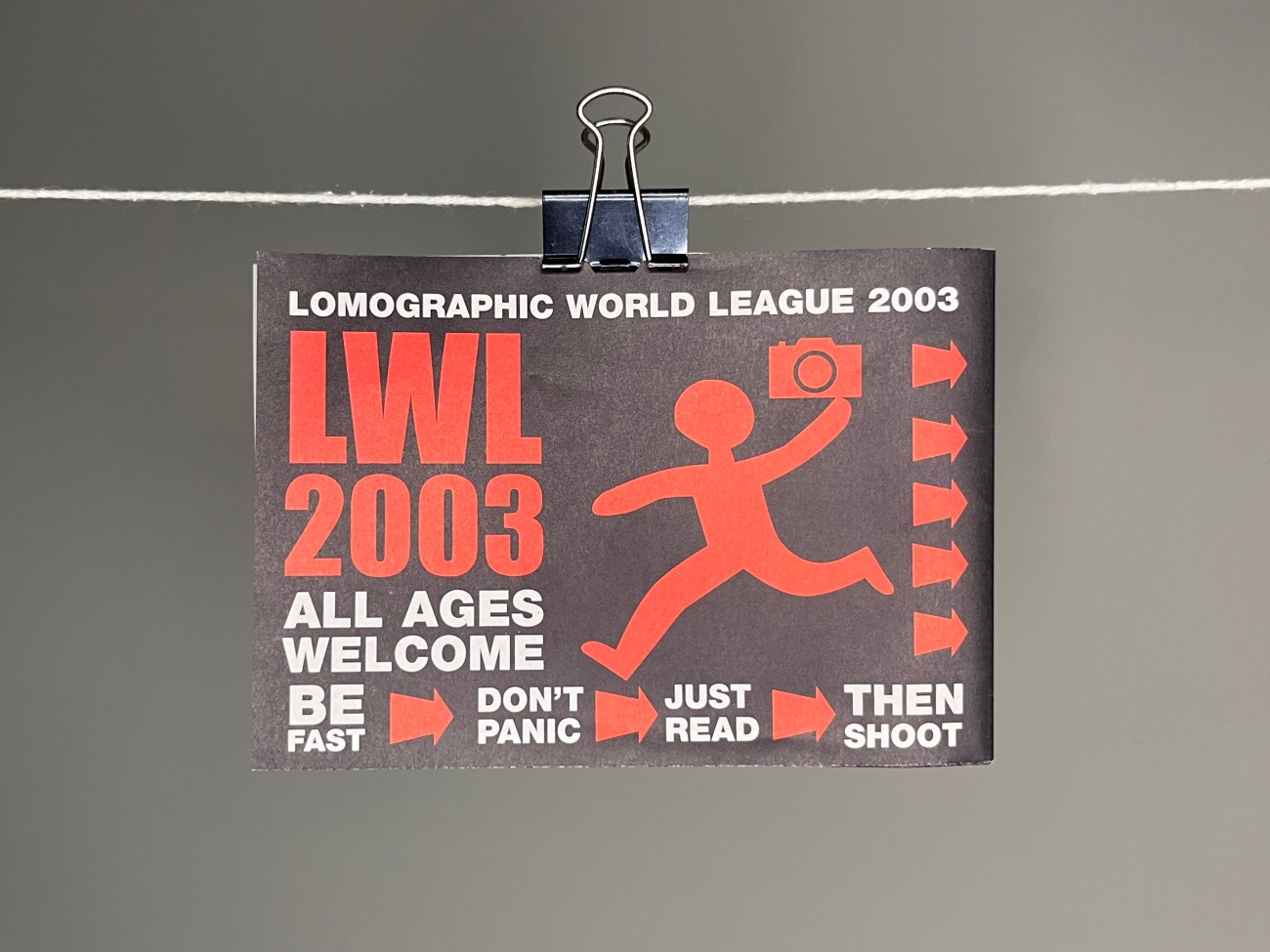 The folded up version of the poster with white and red typography on a black background and an icon of a person holding a camera. Instructions at the bottom of the design say Be fast, don't panic, just read, then shoot.  