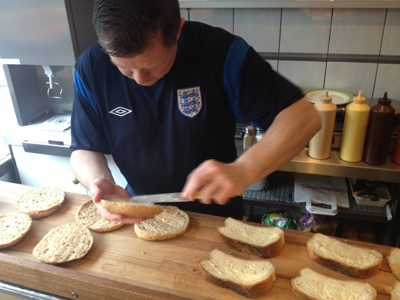 James, the England football top wearing sandwich maker butters bread that's lined up on the counter. 