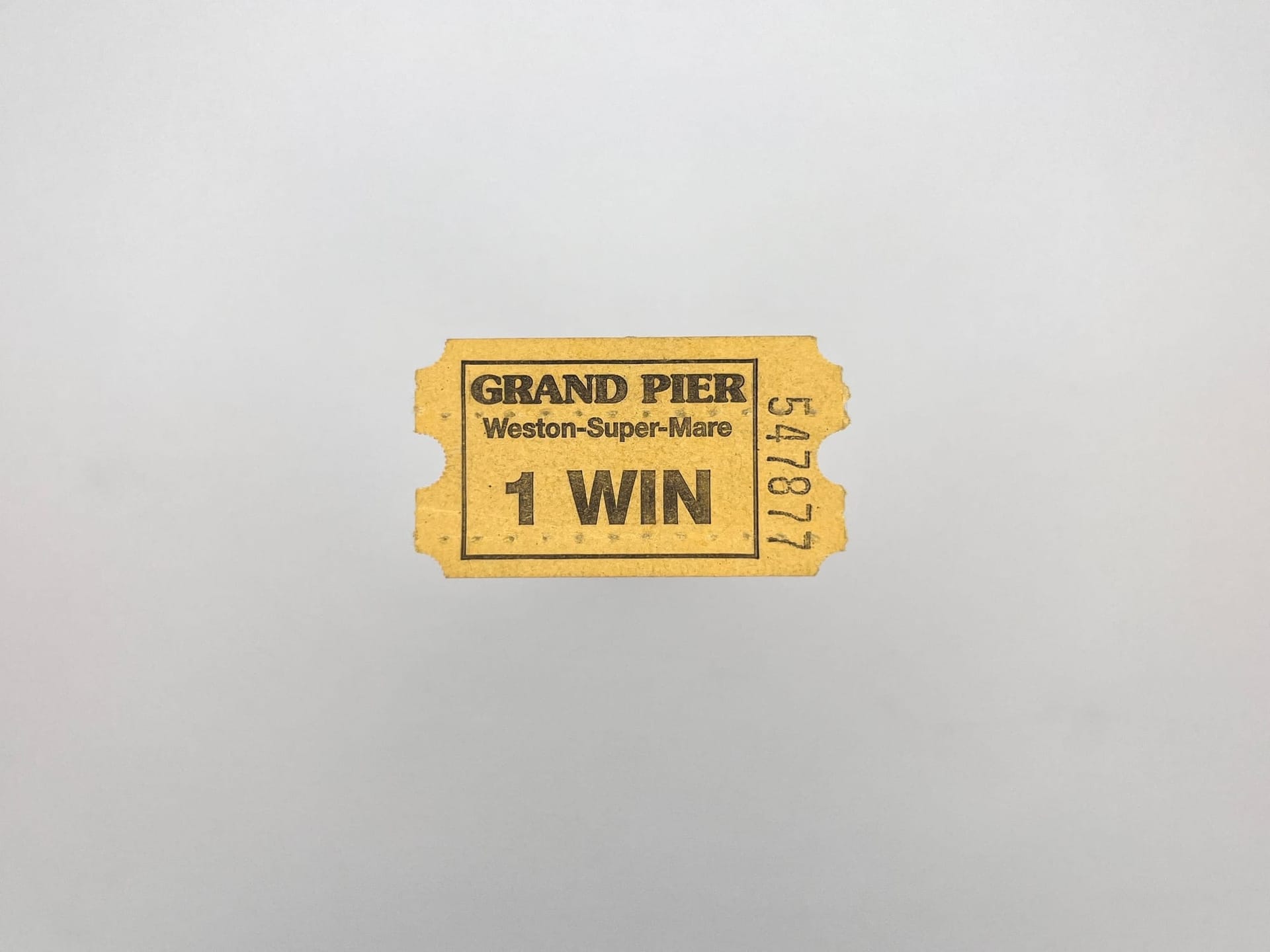 A small yellow paper ticket from a ticket machine. It says Grand Pier, Weston-Super-Mare 1 Win and has the serial number 547877 down the right side